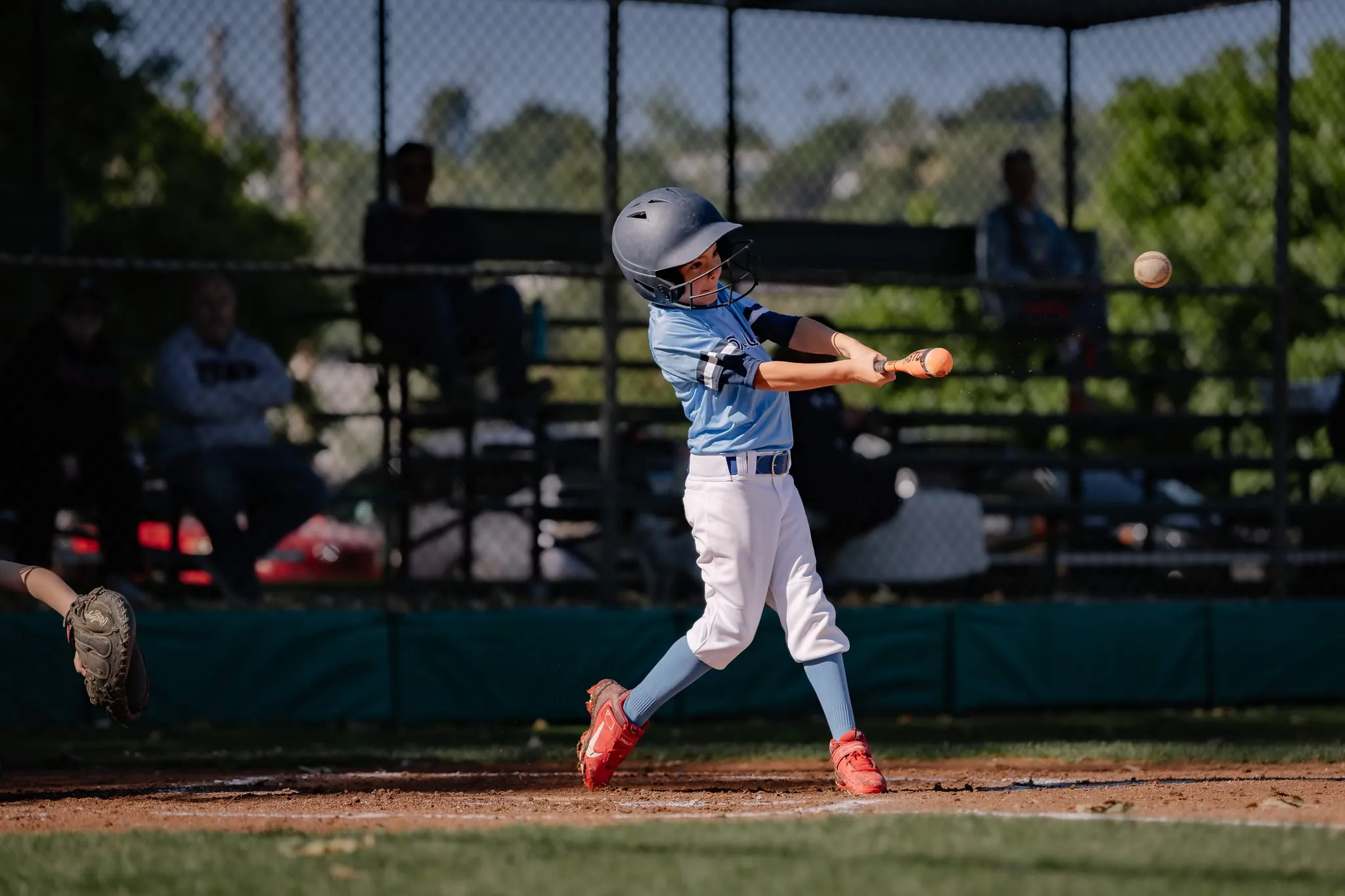 Young batter connects with the pitch, the ball just leaving the bat