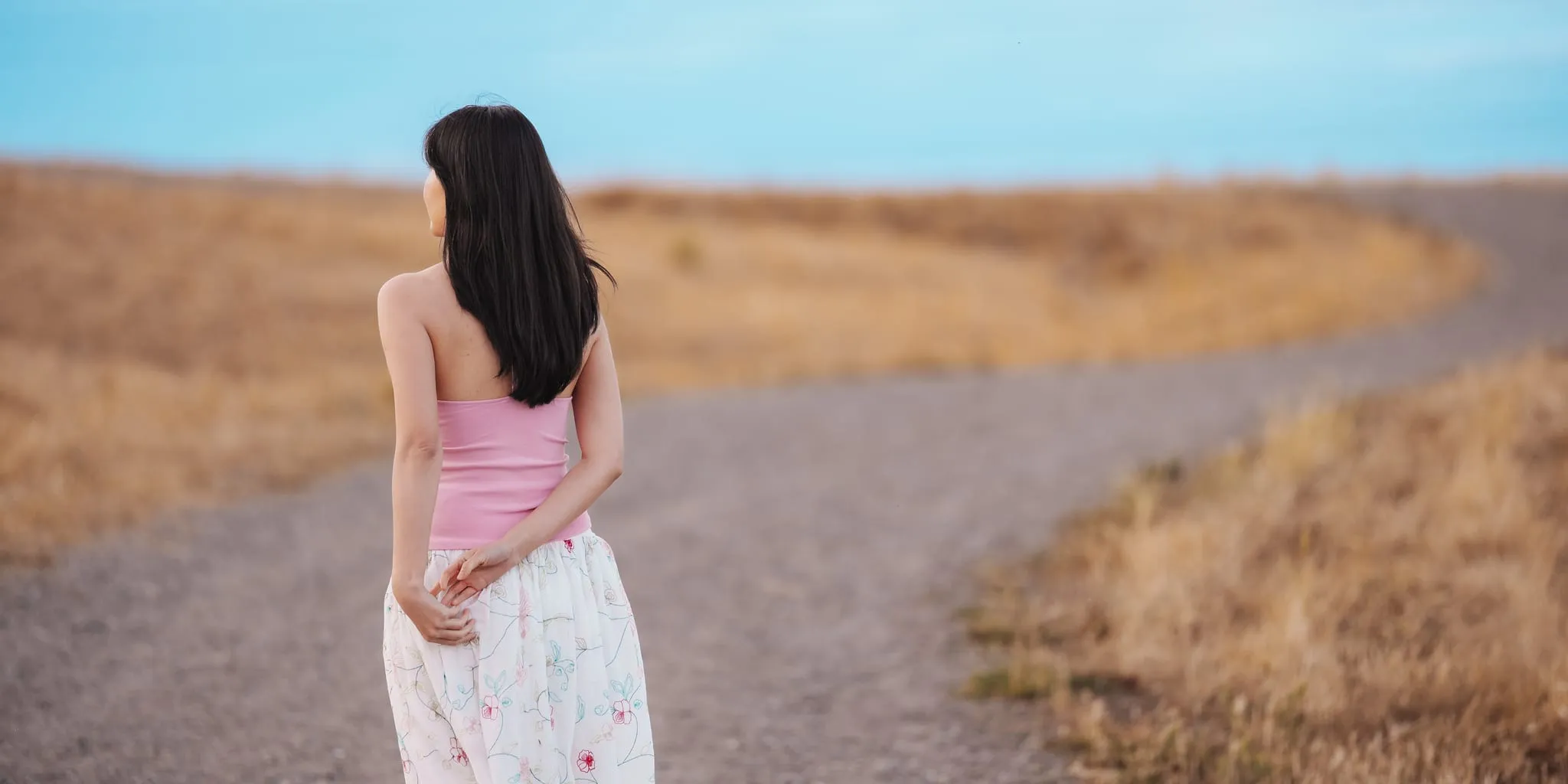 背影:女子驻足于金色草地间弯曲的小径旁