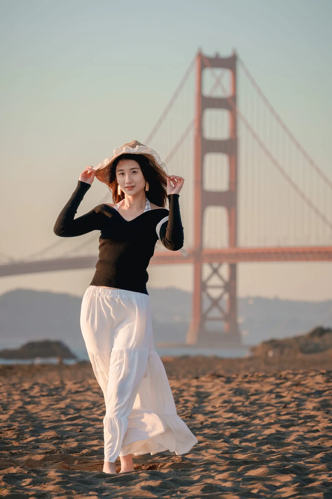 Full-length portrait on Baker Beach sand, white skirt in the breeze, the Golden Gate Bridge rising behind