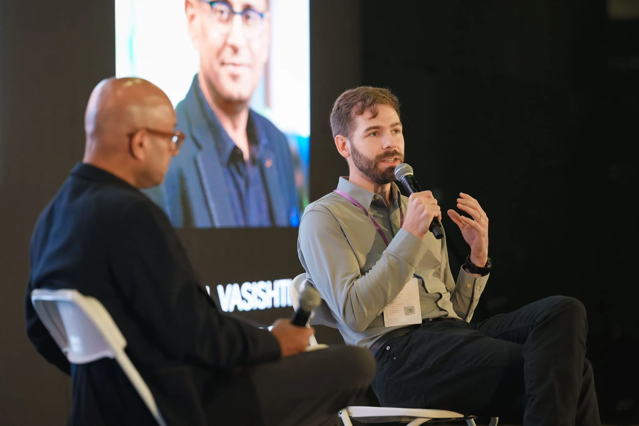 A guest speaks with the mic mid-gesture during a low-lit fireside chat