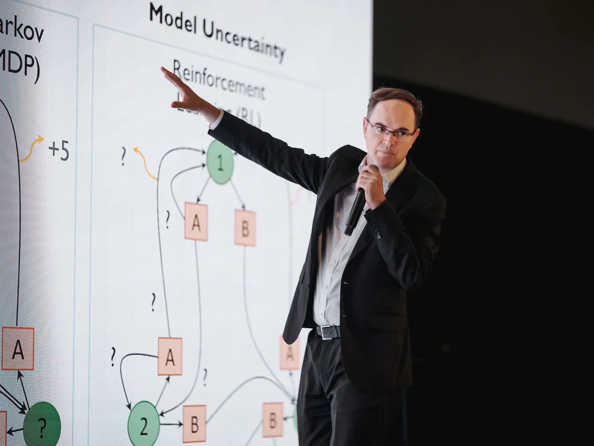 A speaker gestures at a reinforcement-learning diagram during a technical keynote